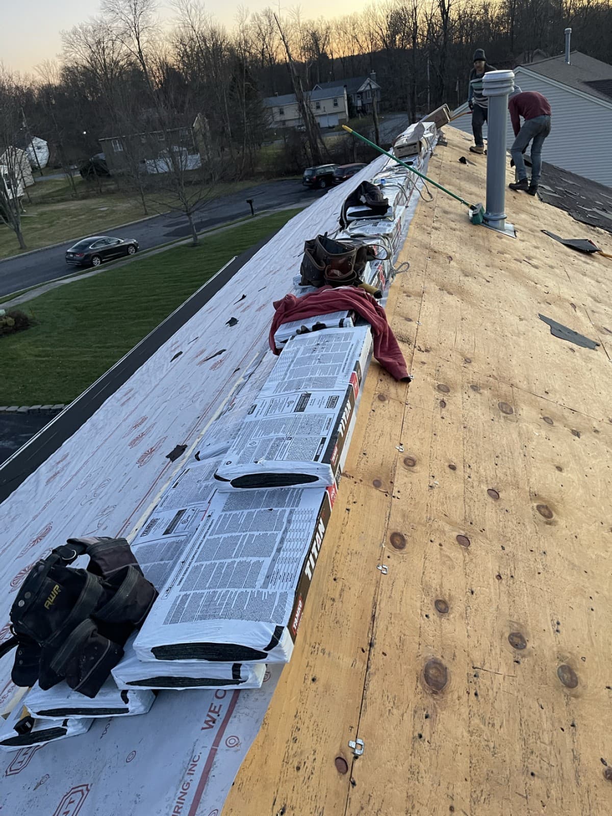 Roofers working beside exposed decking and bundles along the roof ridge