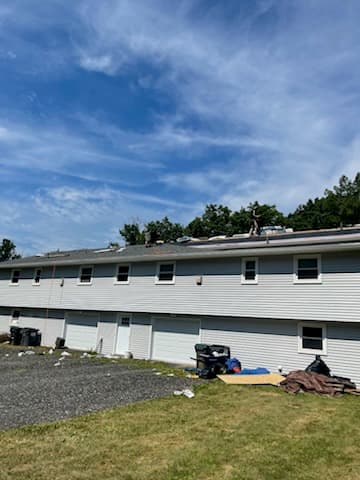 Long two-story house with roofing materials and a tarp beside it