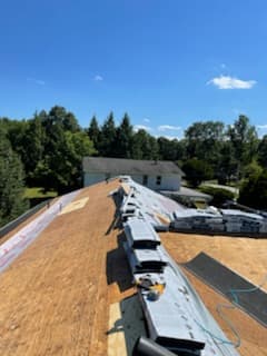 Roof ridge lined with shingle bundles beside exposed decking