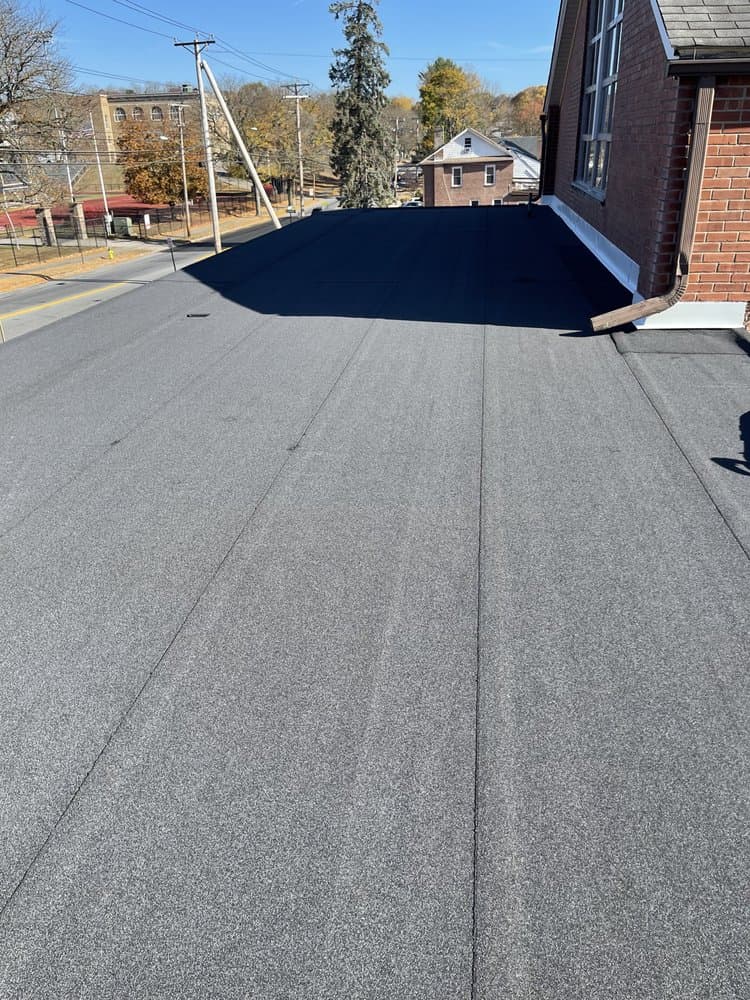 Low-slope roof surface meeting a brick wall with metal flashing