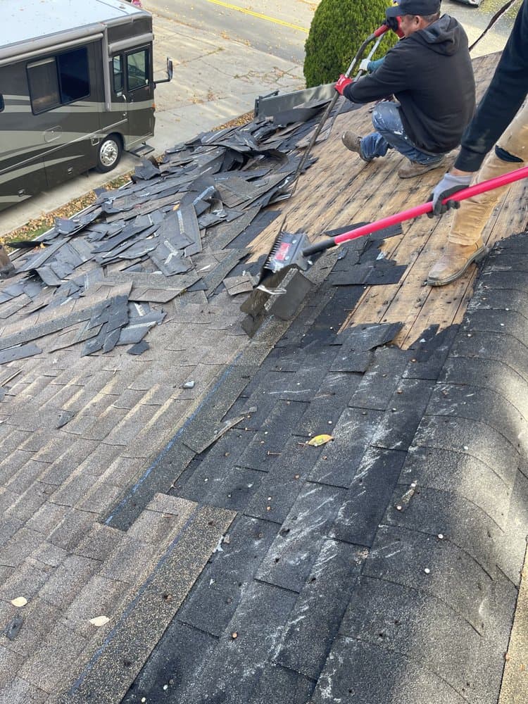 Roofing crew removing old shingles to expose wood decking