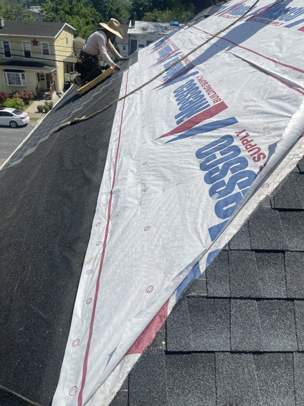 Roofer working where gray shingles meet white underlayment