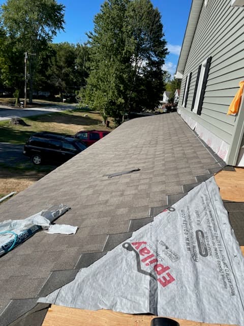 Gray shingles beside white underlayment at a house wall