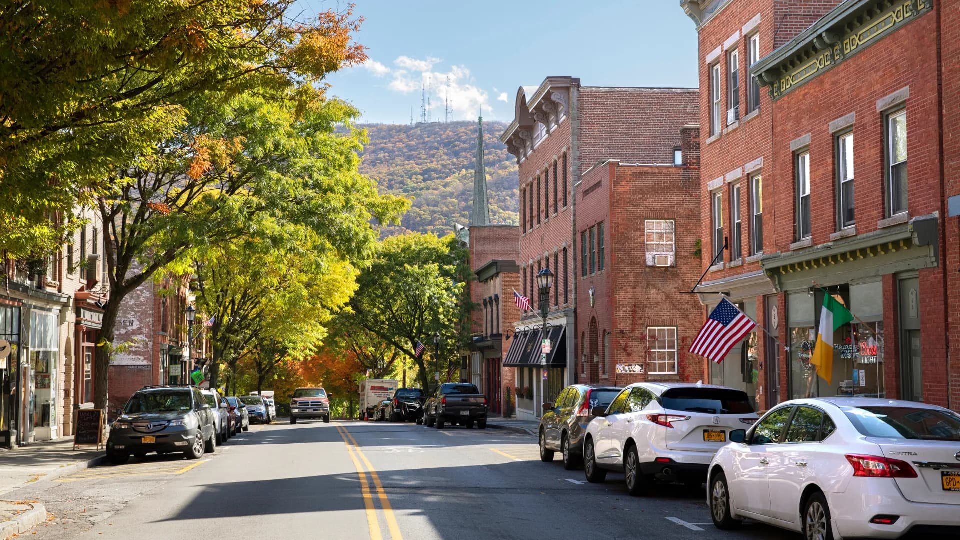 Brick storefronts along a tree-lined street with a mountain in the distance