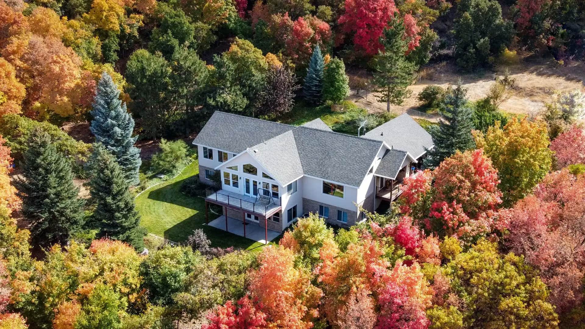 White house with a gray shingle roof surrounded by autumn trees