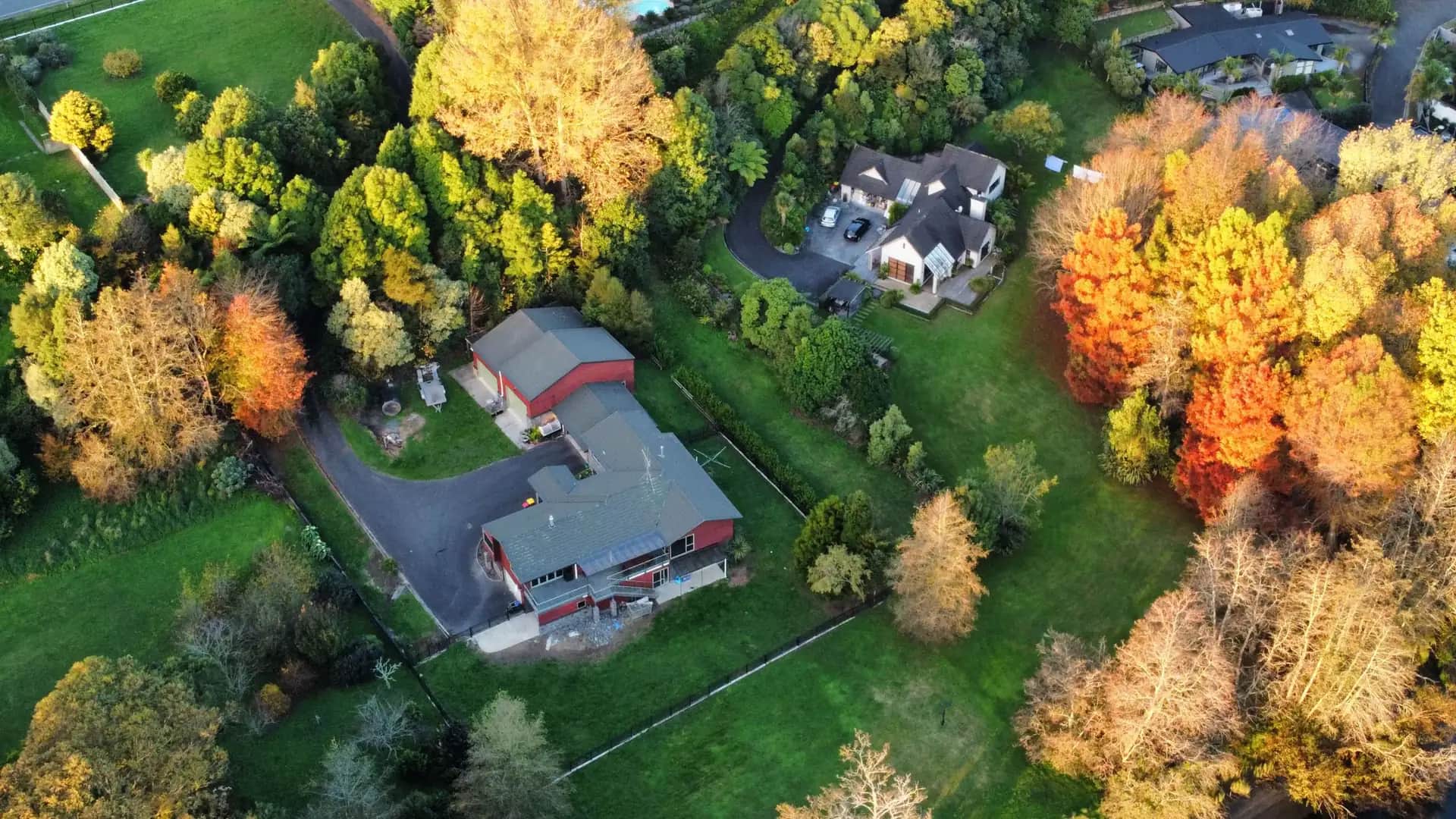 Aerial view of homes, a red barn, and lawns among autumn trees