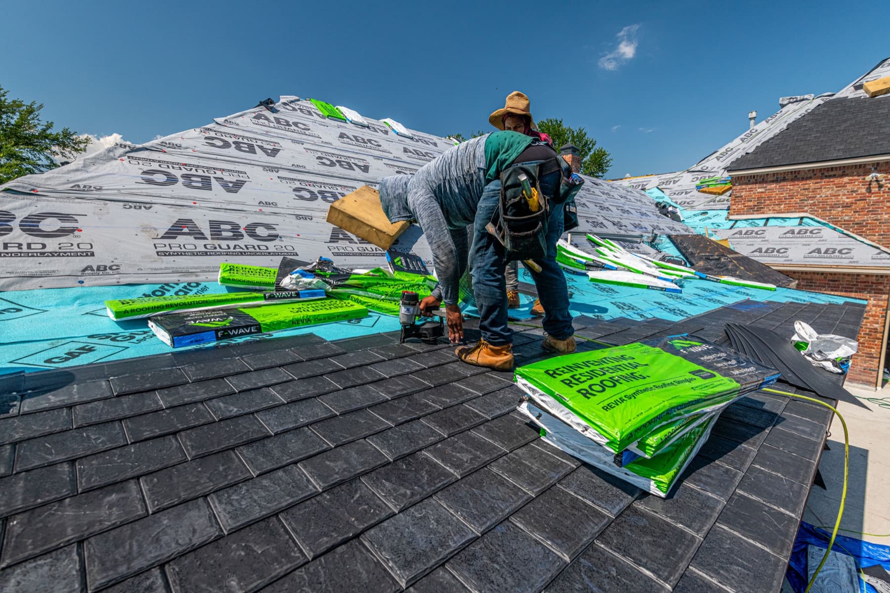 Roofer installing shingles beside underlayment and stacked shingle bundles
