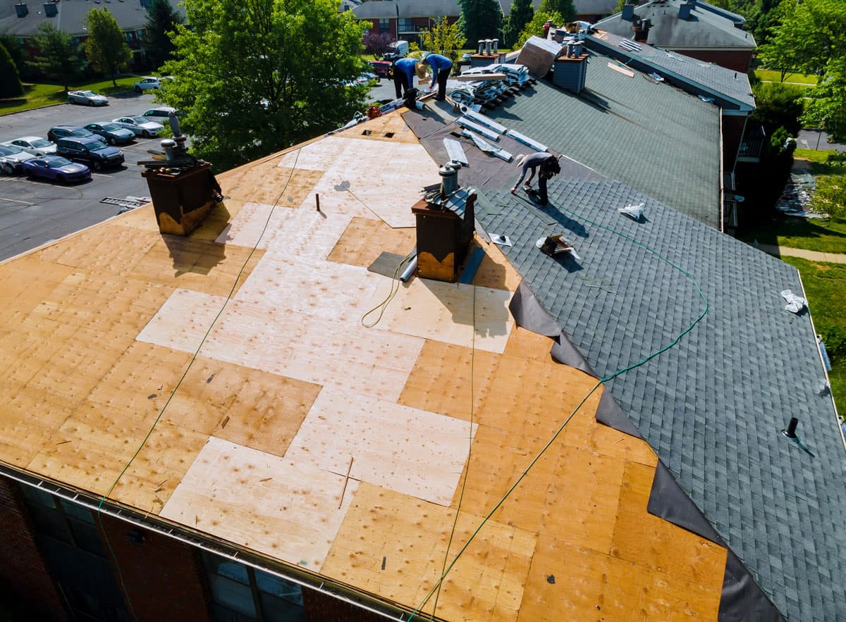 Roofing crew beside exposed wood decking during roof replacement