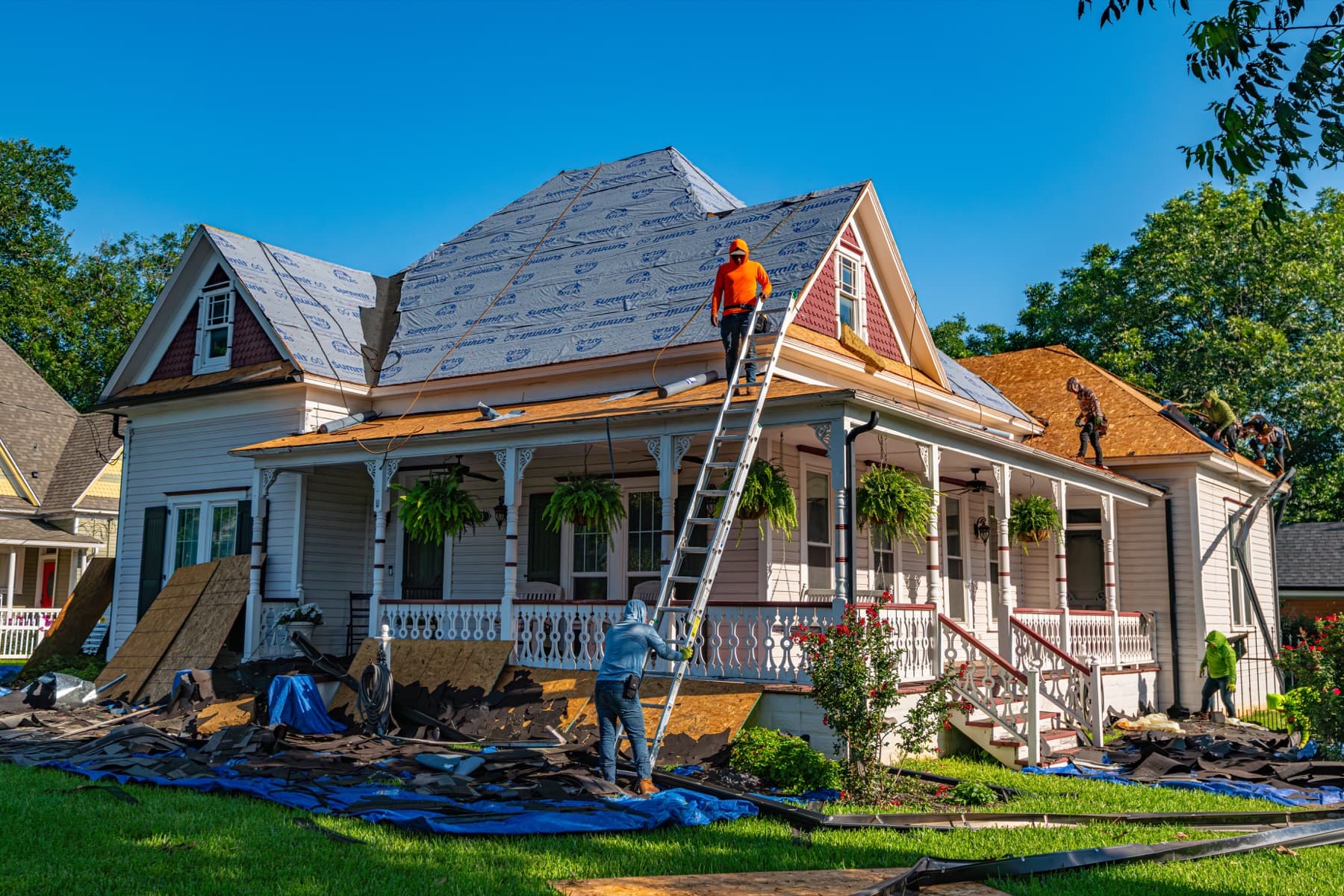 Roofers working on the roof of a two-story house with a front porch