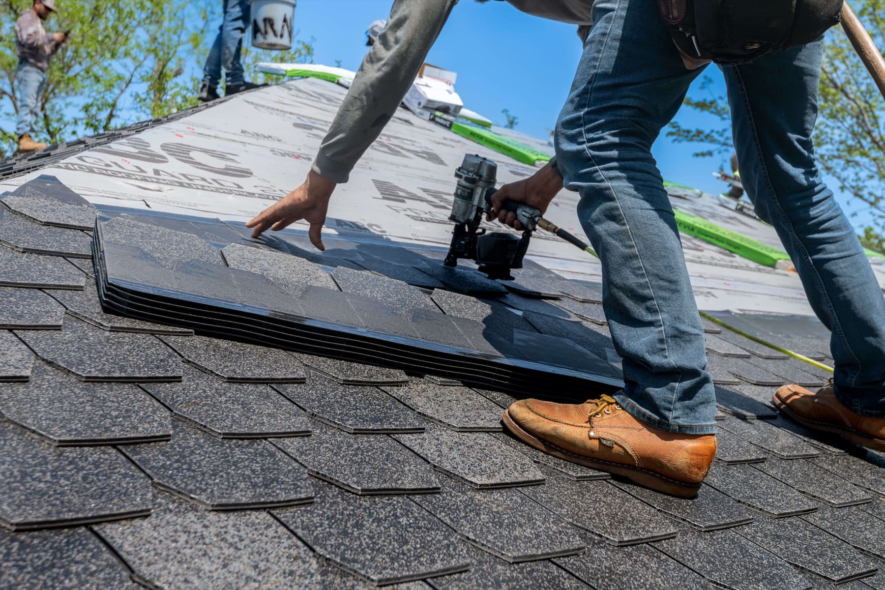 Roofer positioning a shingle with a roofing nail gun